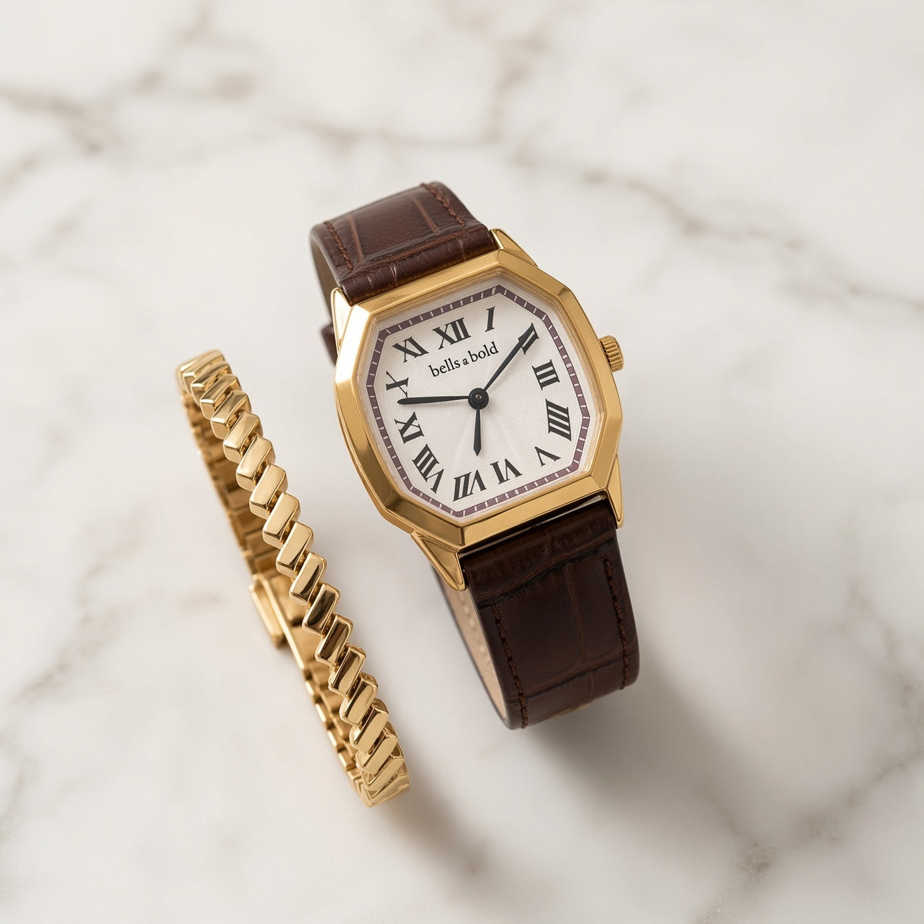 A gold-tone watch with an octagonal bezel, white dial, black Roman numerals, and a brown leather strap, displayed next to a matching gold chain bracelet on a white marble surface.